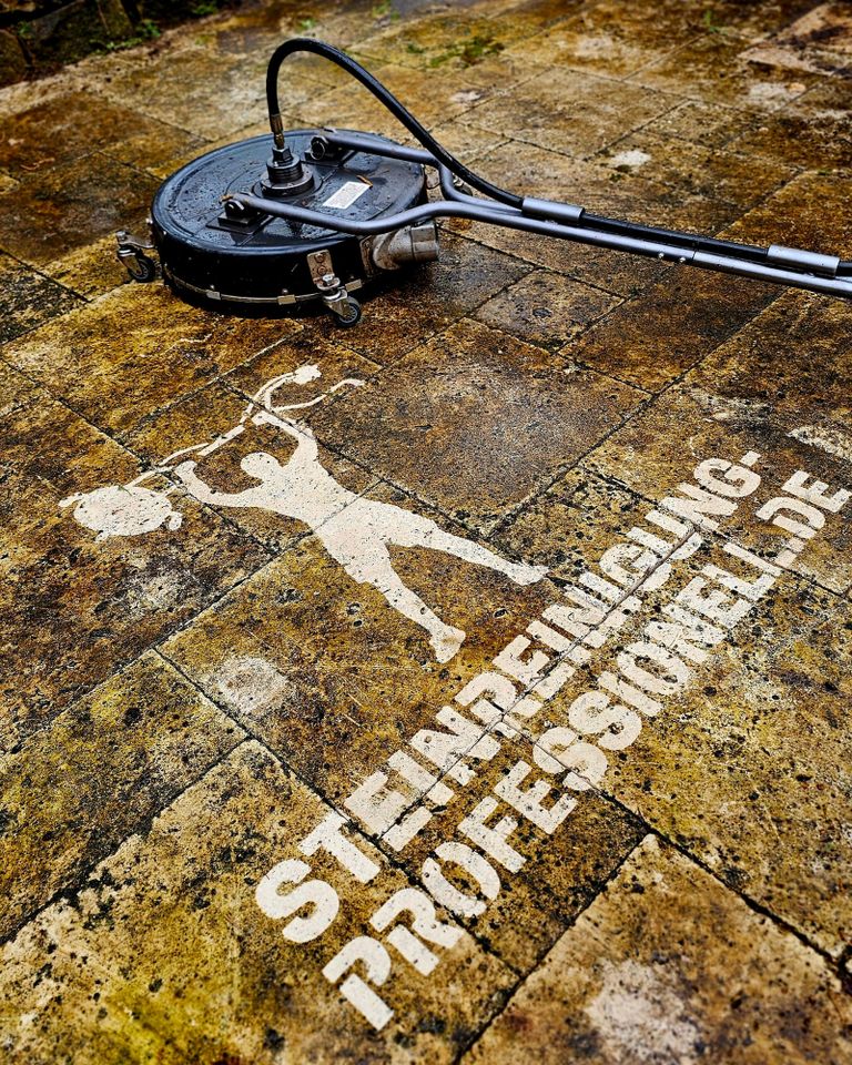 "Professionelle Steinreinigung mit Hochdruckreiniger, zeigt das Firmenlogo durch Schablonentechnik auf der gereinigten Fläche