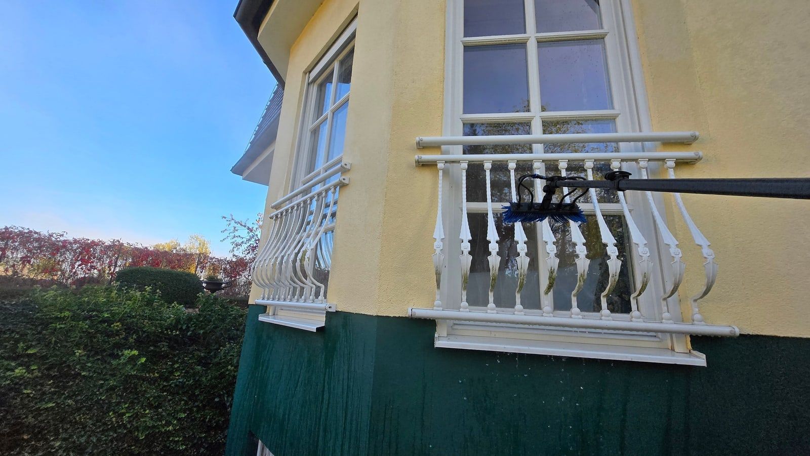Blaue Reinwasserbürste reinigt ein Sprossenfenster an einer historischen Villa