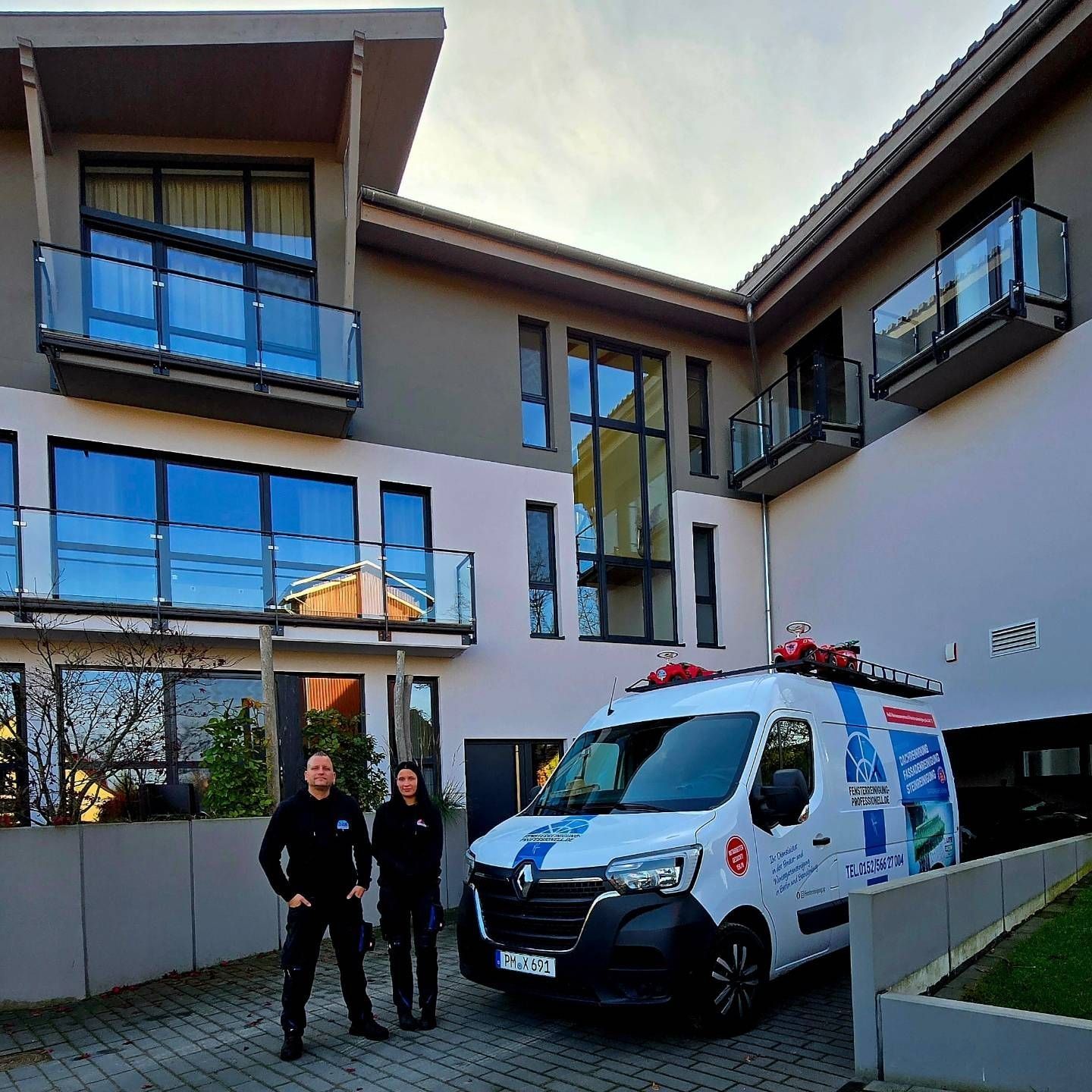 Zwei Mitarbeitende der Fensterreinigung Professionell vor dem Firmenfahrzeug an einem modernen Mehrfamilienhaus