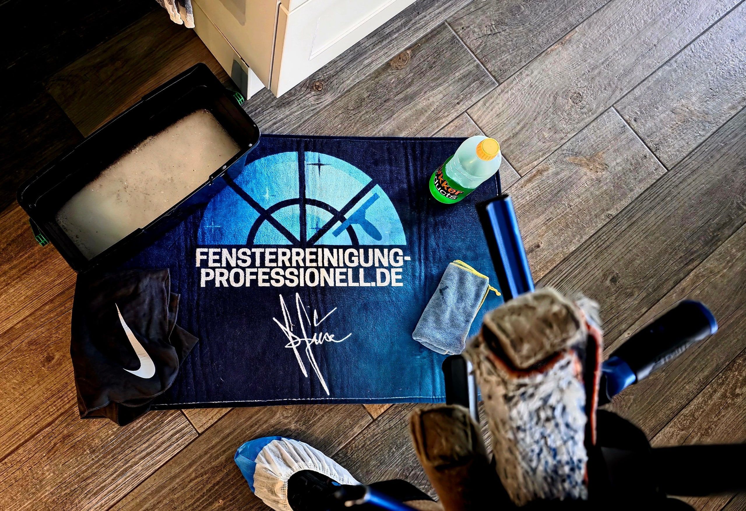 Firmenmatte mit Putzeimer, Mikrofasertuch und Reinigungsmittel im Eingangsbereich eines Kundenhauses