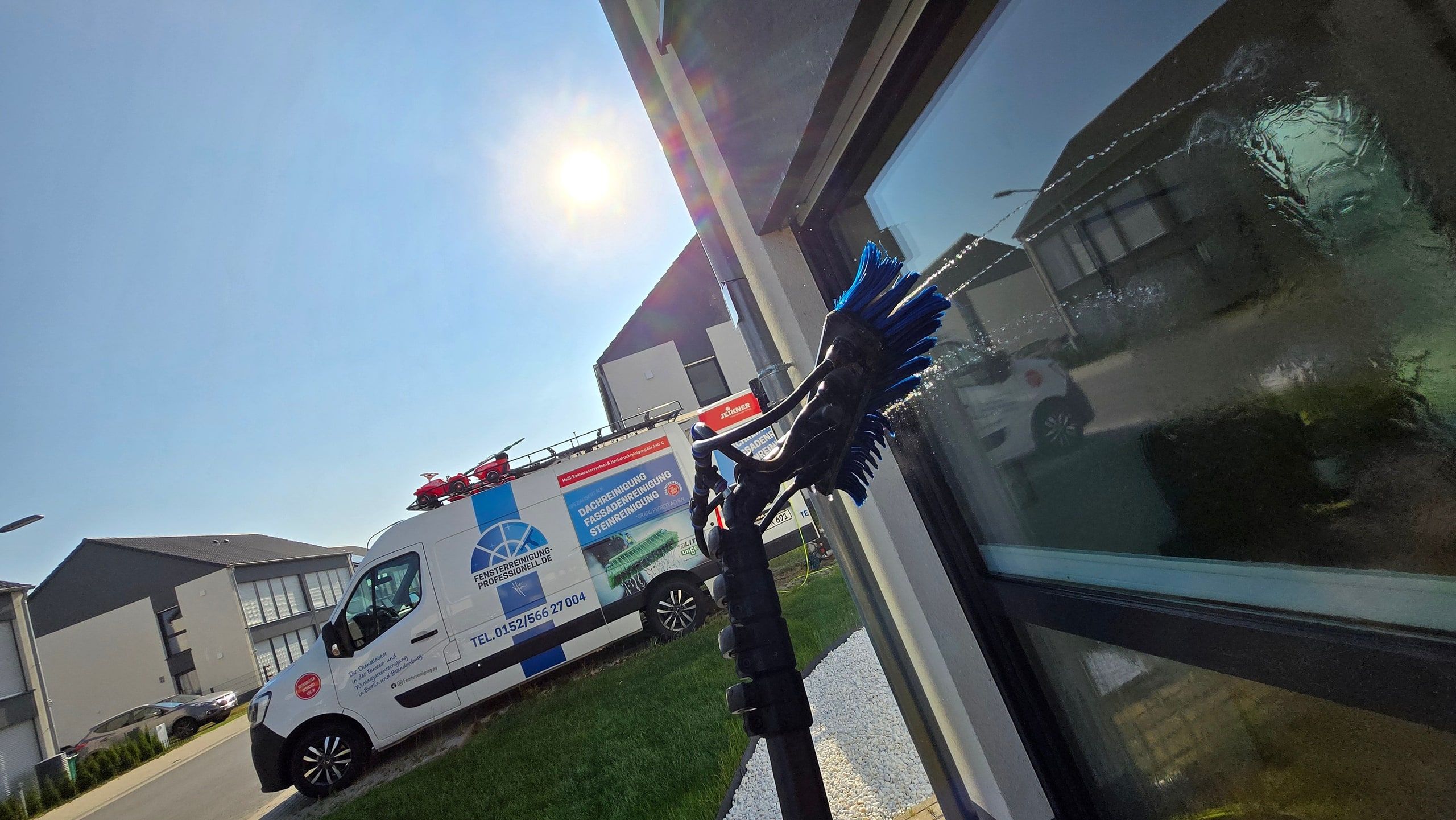 Reinwasserbürste reinigt ein Fenster, dahinter das Firmenfahrzeug in einem Wohngebiet in Ludwigsfelde