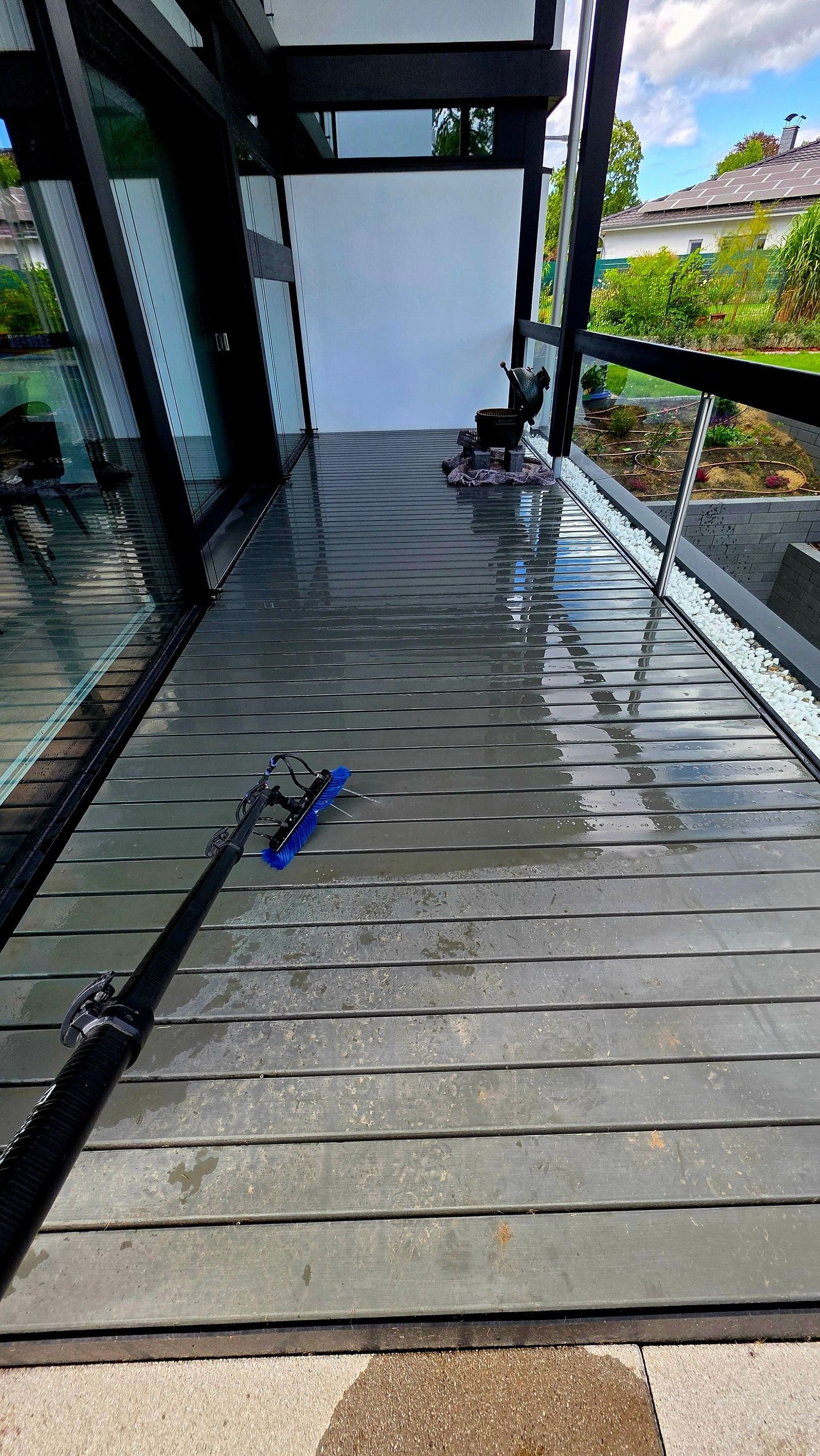 Teleskopstange mit Bürste auf einer frisch gereinigten Terrasse mit Glasgeländer in Stahnsdorf