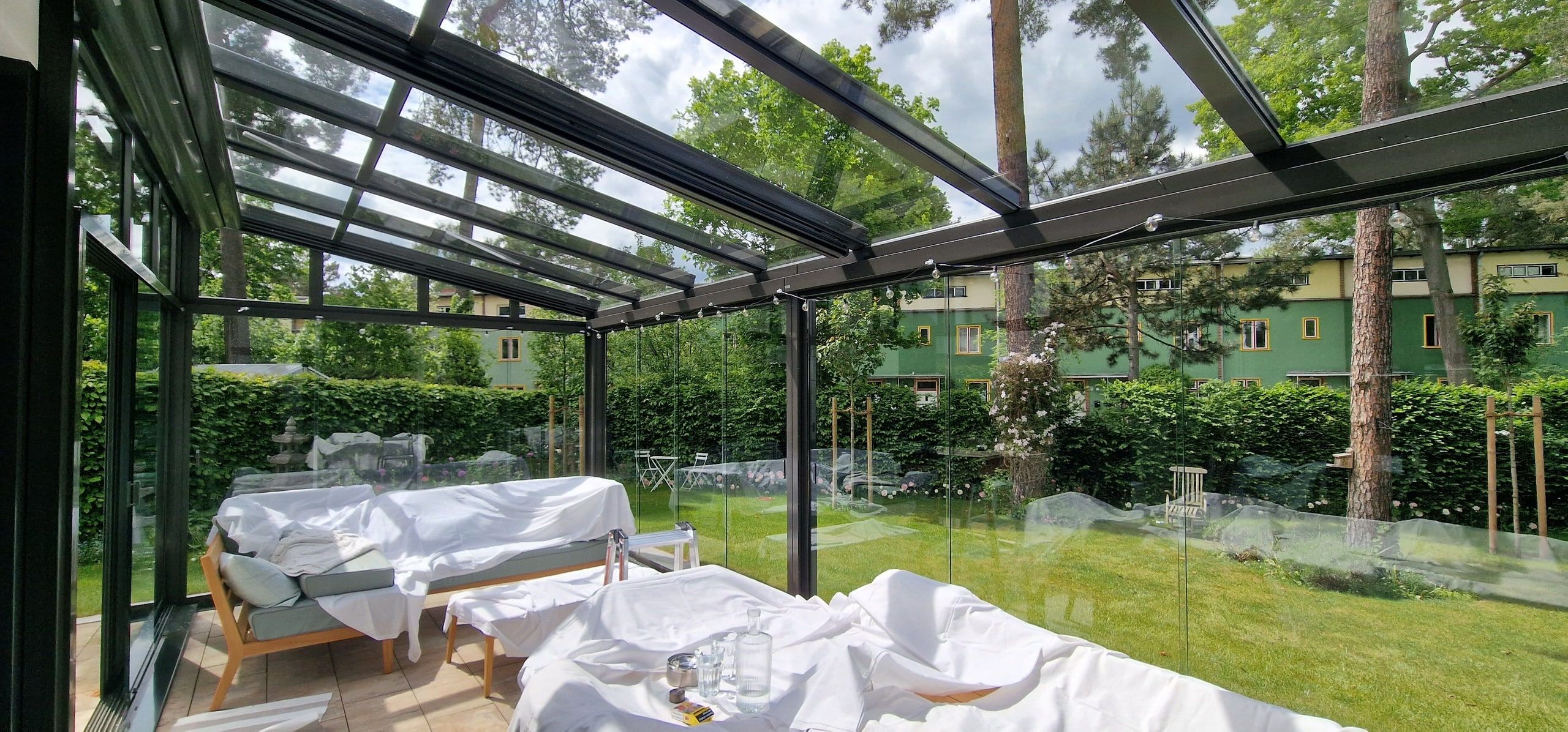 Wintergarten mit abgedeckten Möbeln während der Reinigung, Blick in den Garten