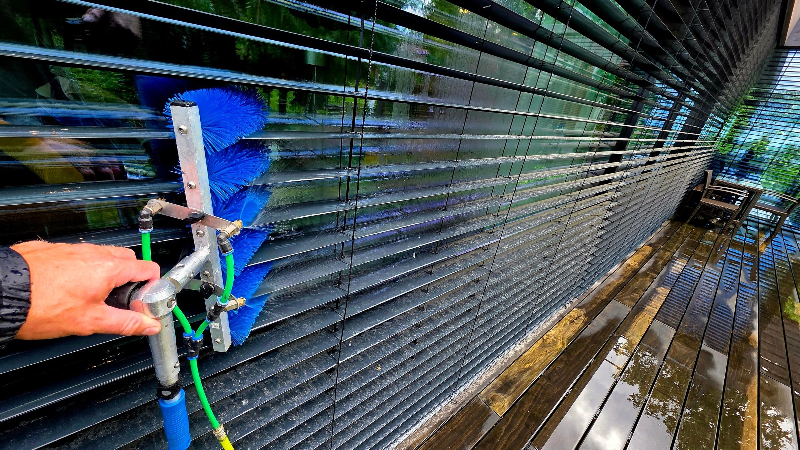 Blaue Bürste reinigt die Lamellen einer dunklen Außenjalousie