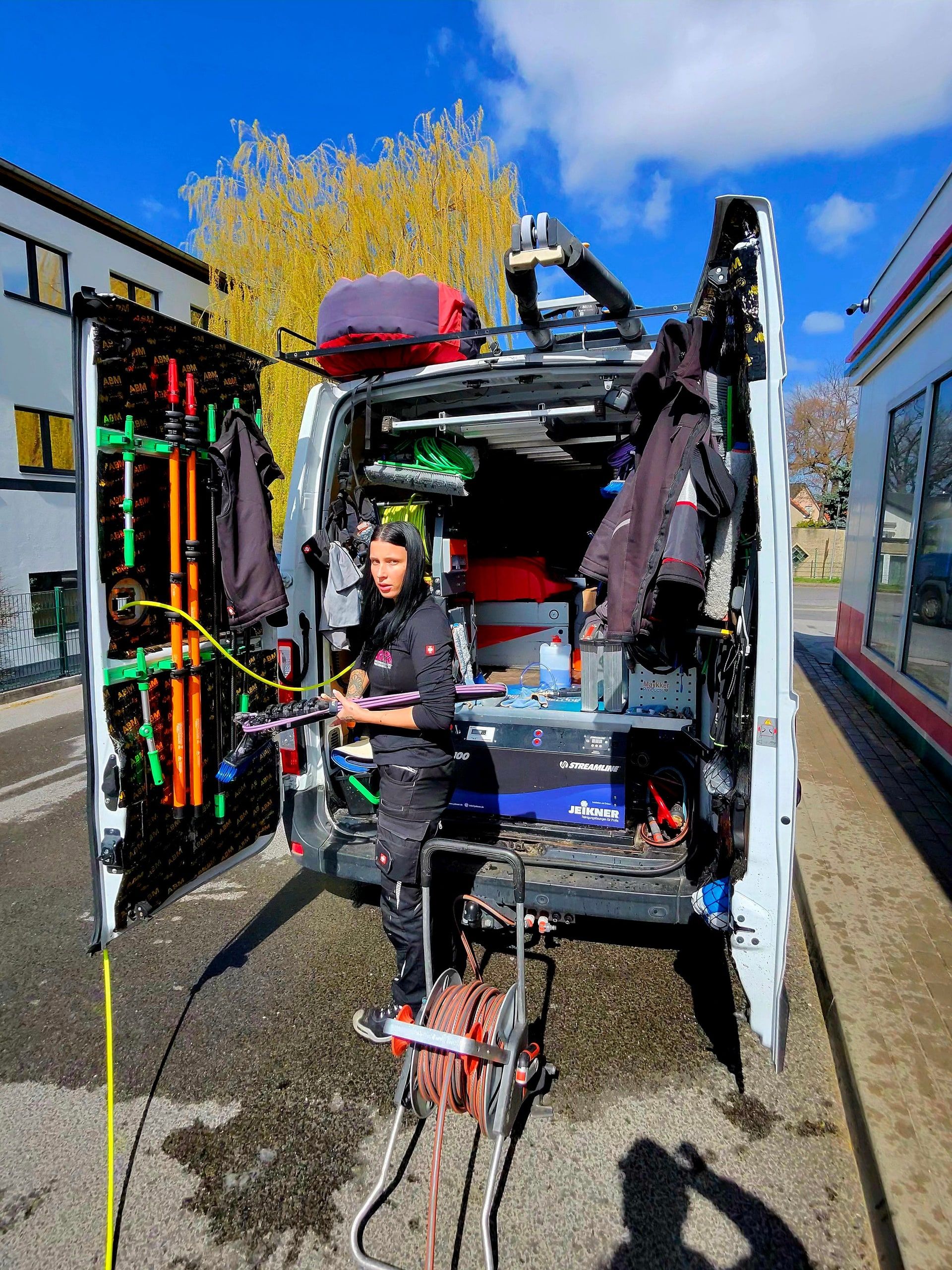 Annabell rüstet sich am geöffneten Fahrzeugheck mit Reinigungswerkzeug aus
