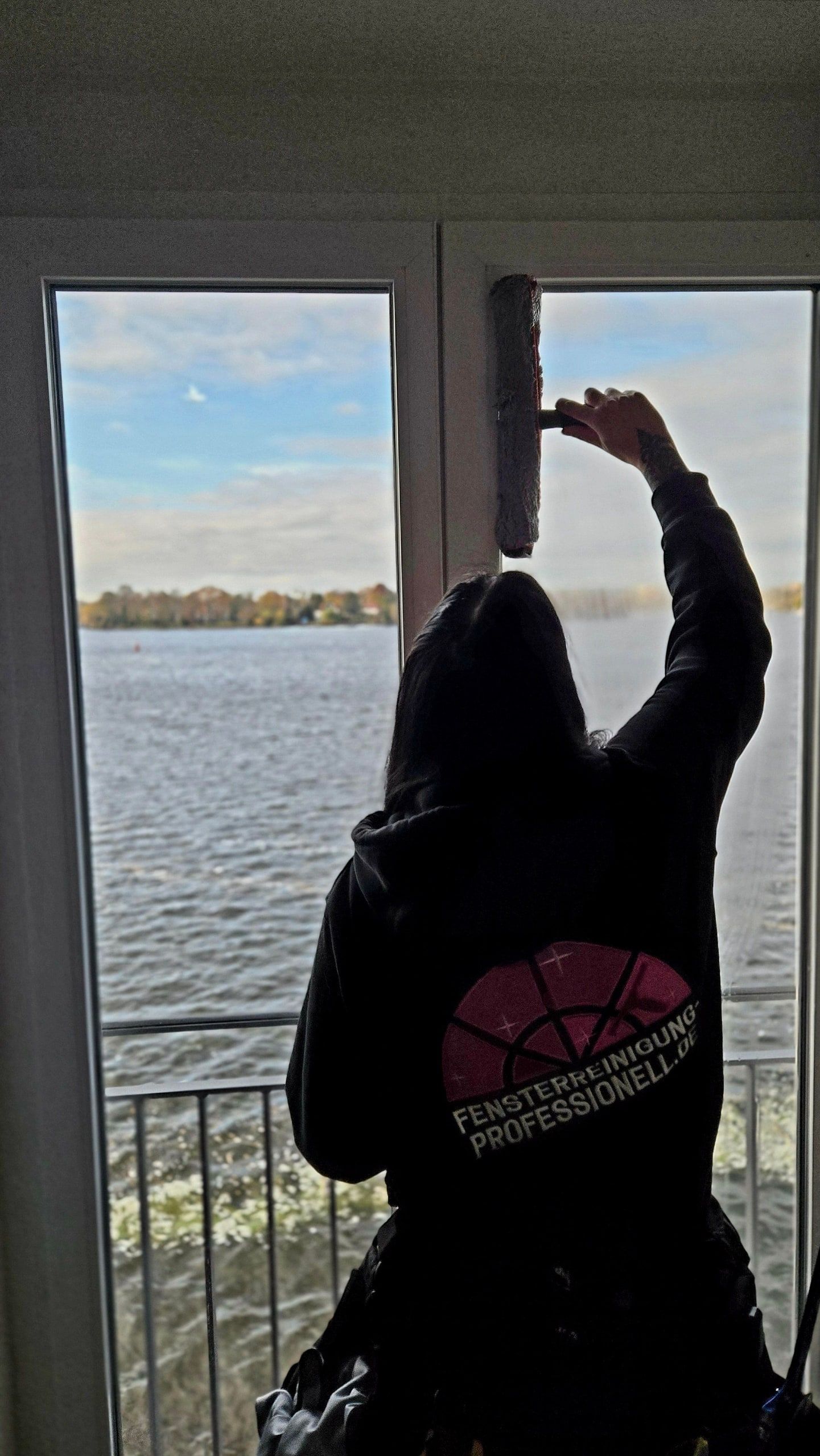 Mitarbeiterin der Fensterreinigung Professionell zieht ein Fenster mit Blick über den See ab