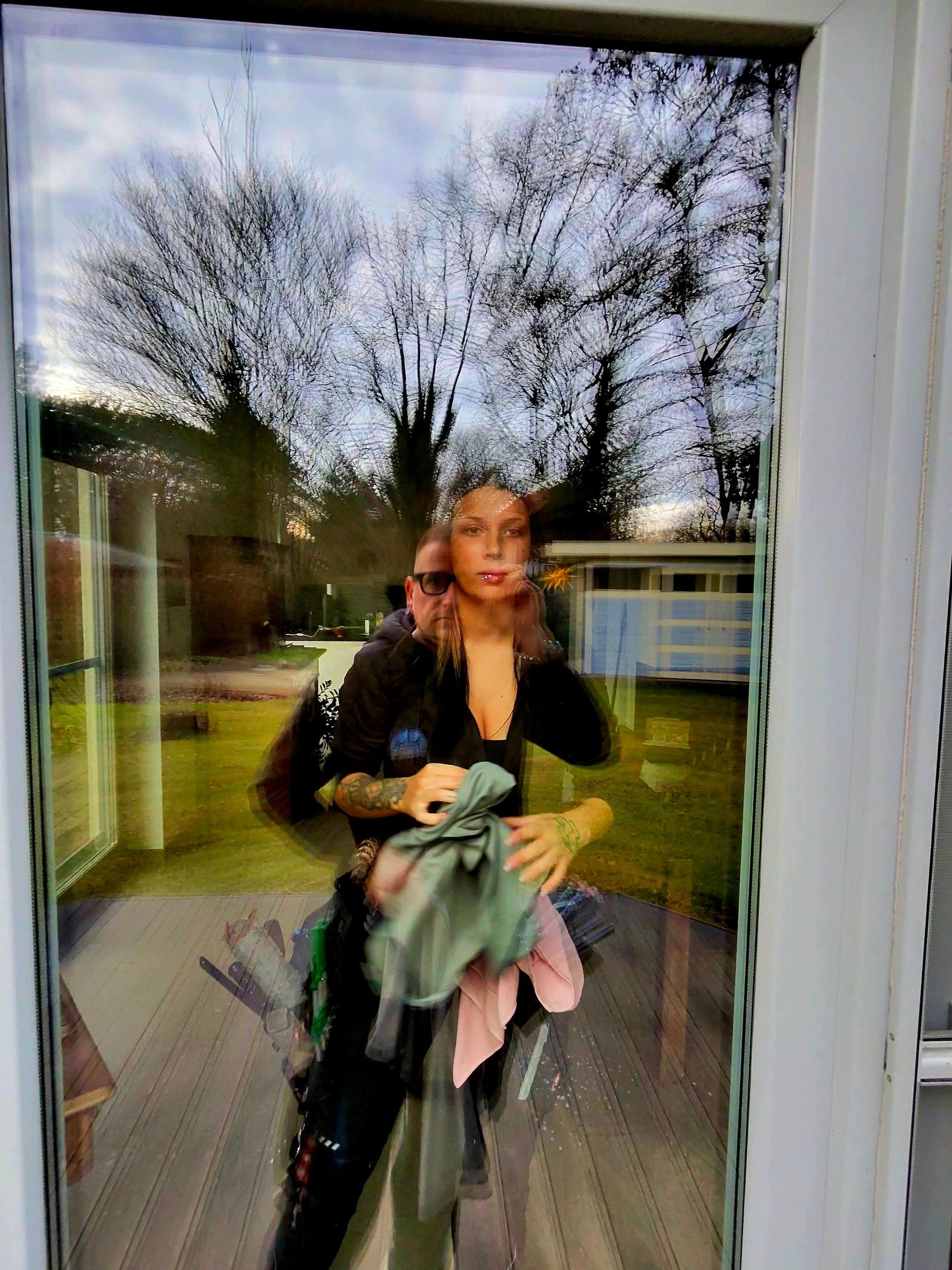 Blick durch eine frisch gereinigte Glastür auf zwei Mitarbeitende mit Reinigungstuch