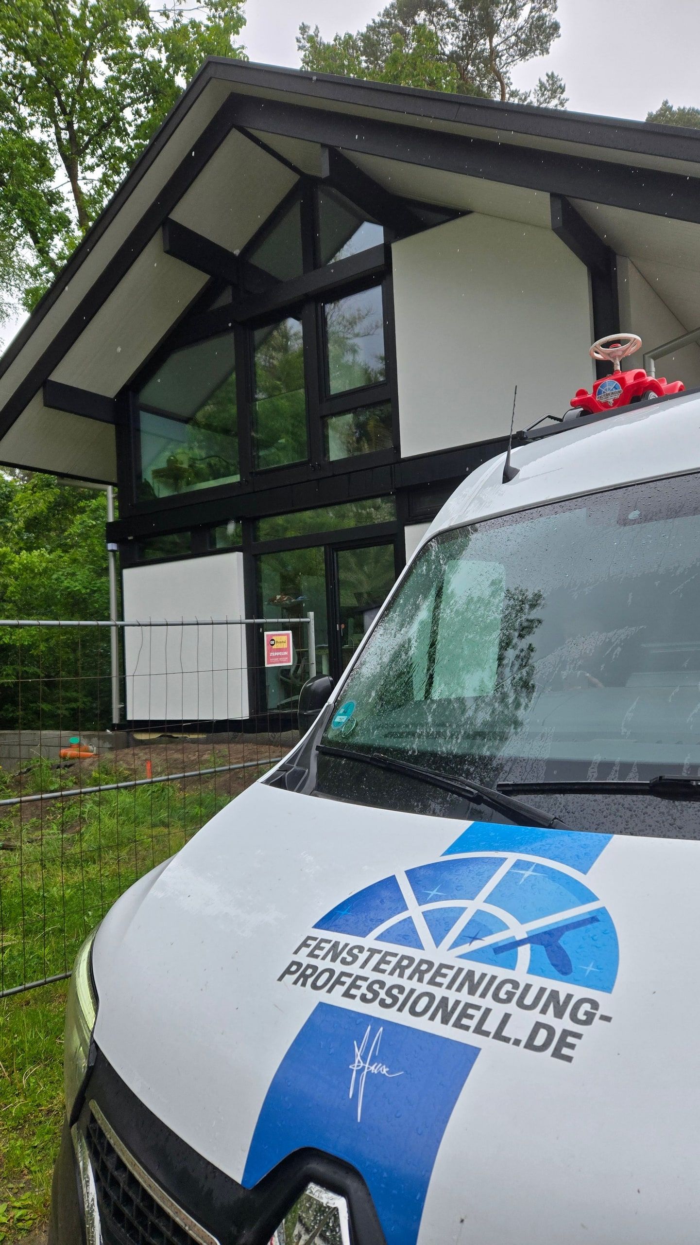Firmenfahrzeug vor einem Wohnhaus mit großer Glasfront