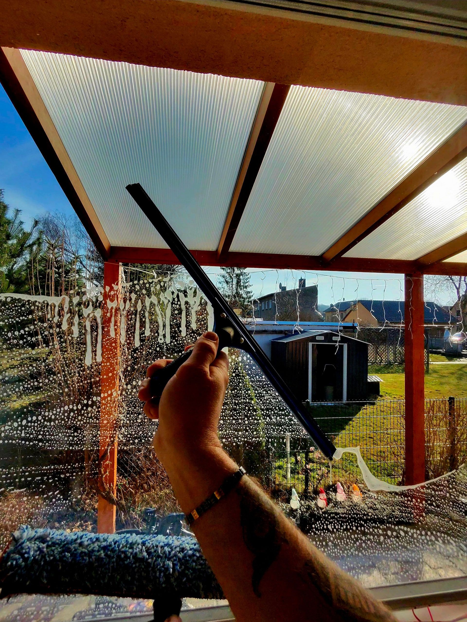 Abzieher reinigt die Verglasung einer Terrasse mit Blick in den Garten
