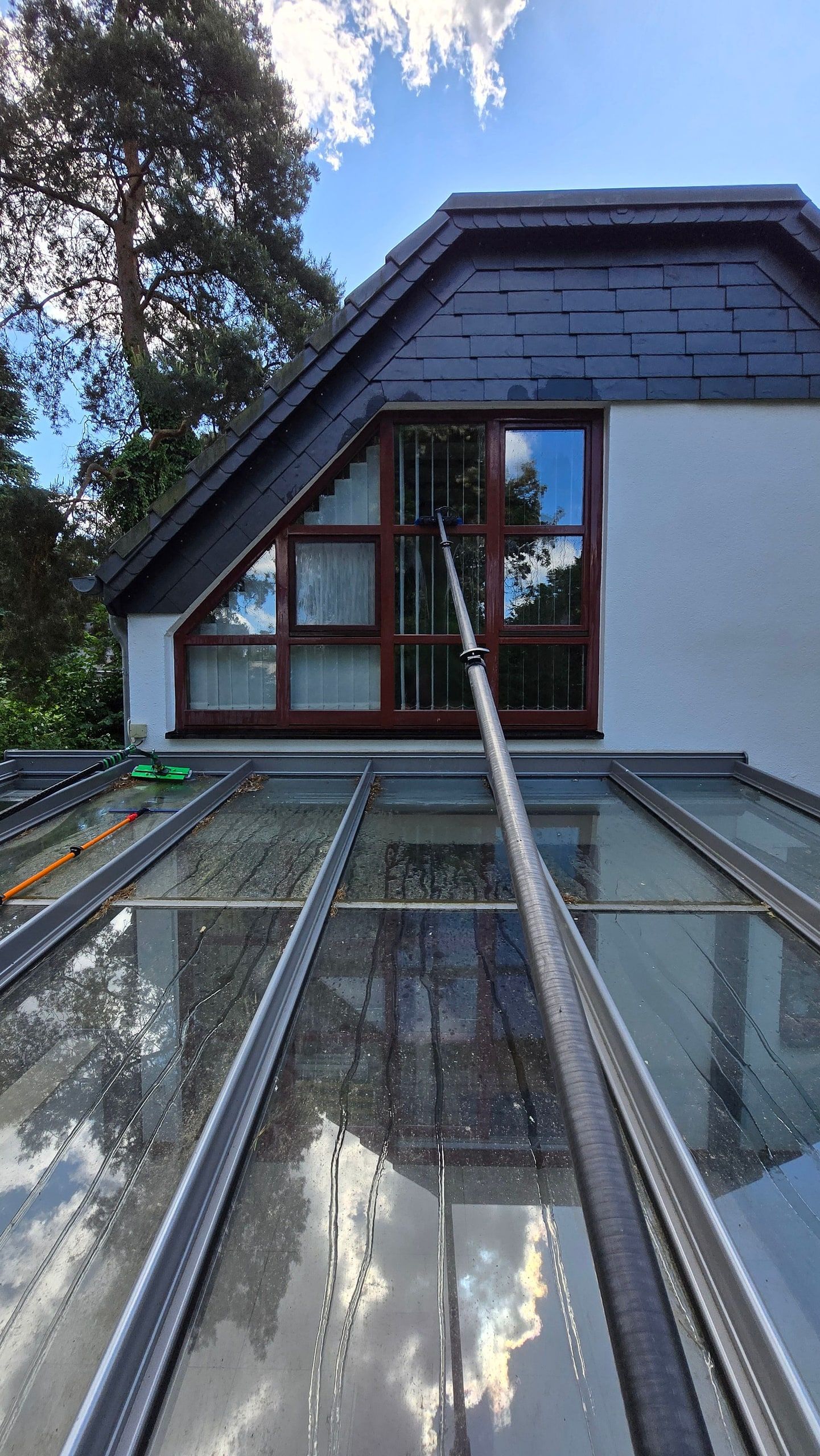 Teleskopstange reinigt das Glasdach eines Wintergartens an einem Landhaus