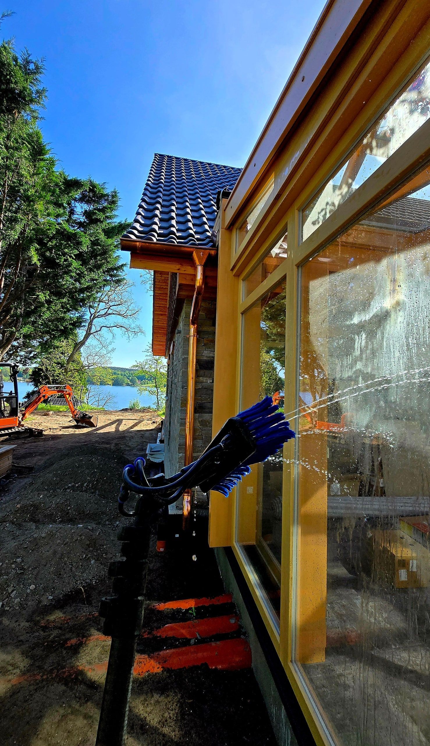 Reinwasserbürste reinigt die Glasfront eines Holzwintergartens am Wasser