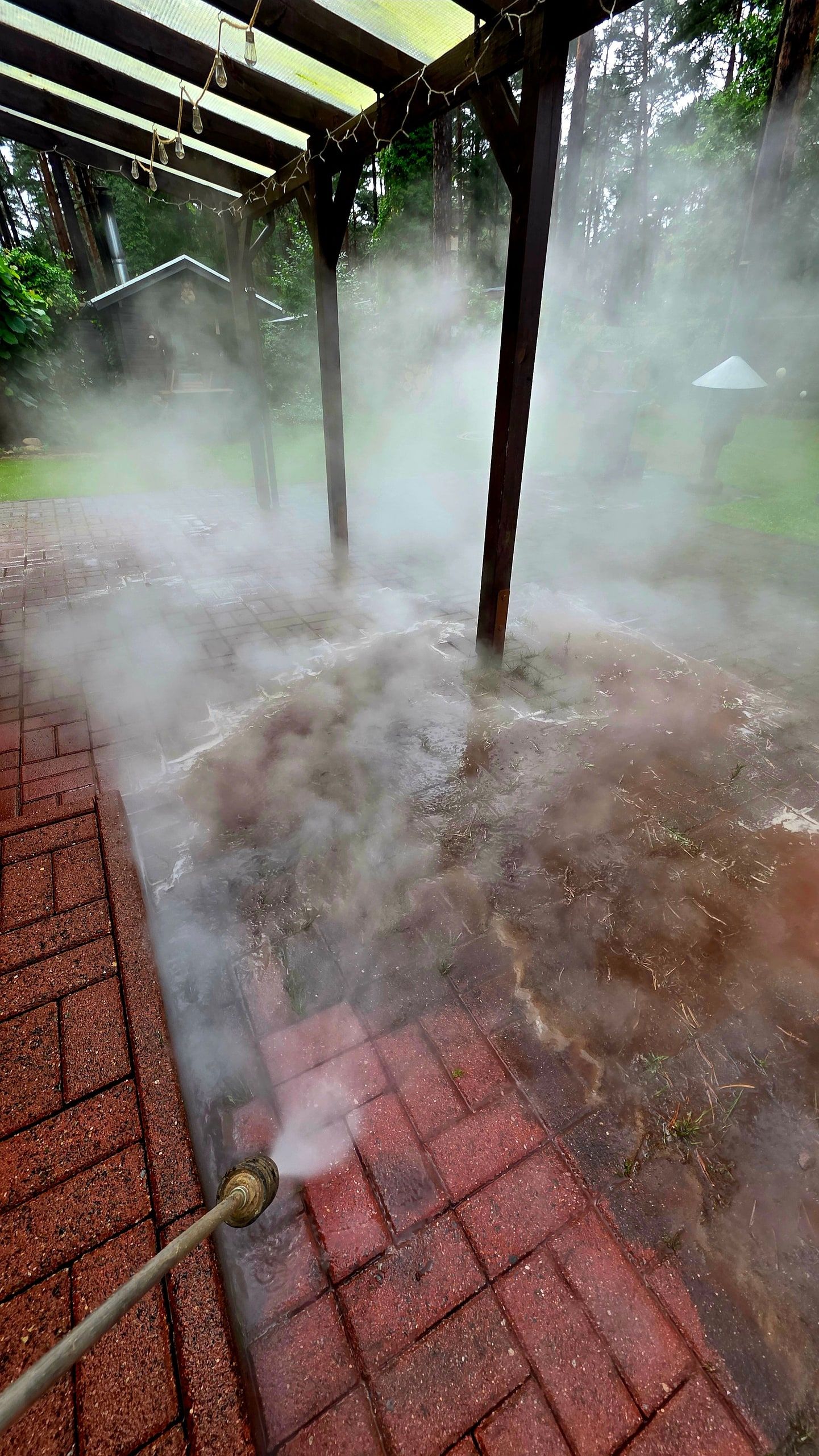 Heißwasserreinigung einer Klinkerterrasse unter einer Pergola, dichter Wasserdampf