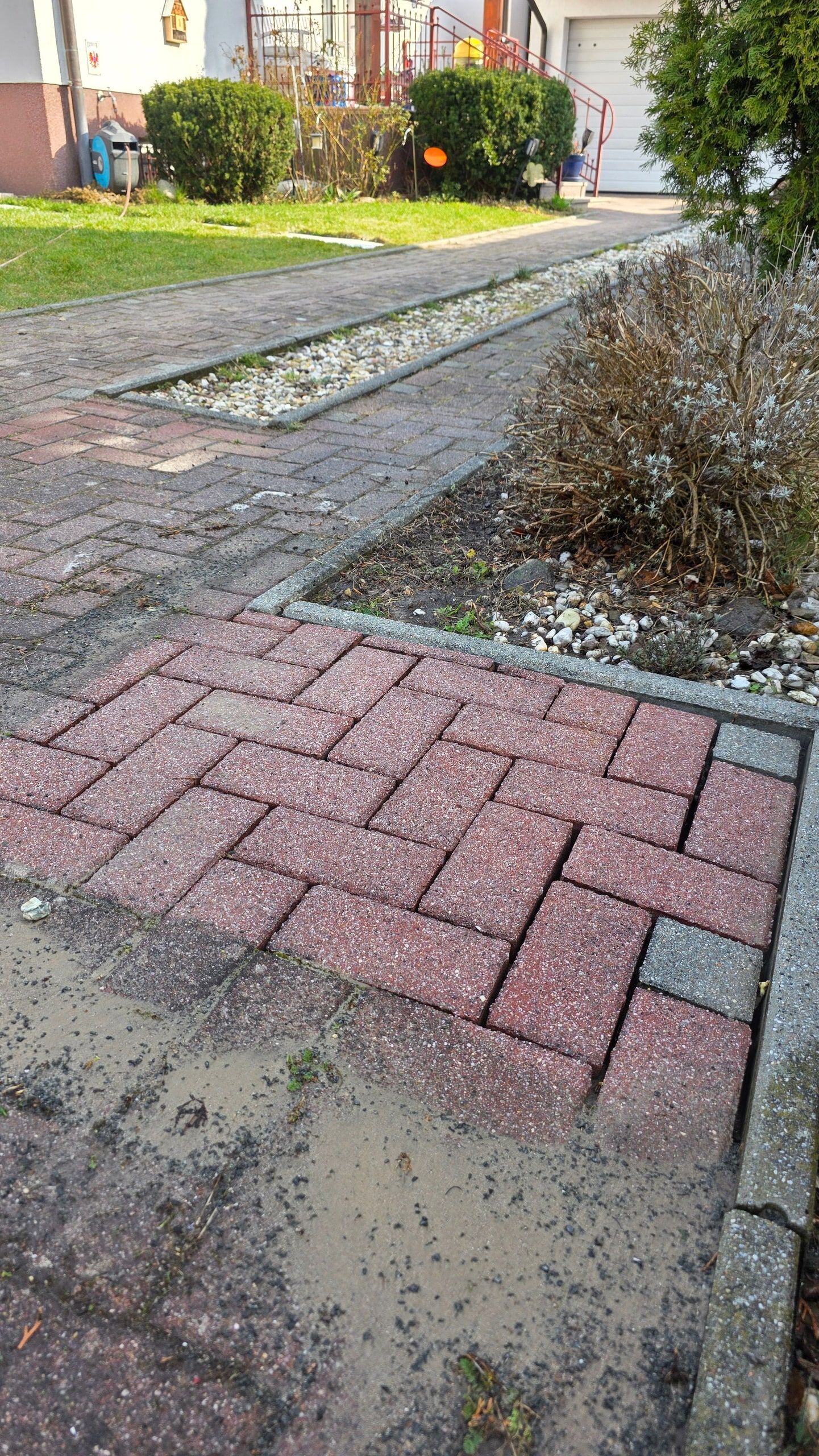 Gereinigter roter Plattenweg entlang eines Beets neben der ungereinigten Fläche