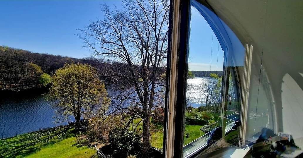 Klarer Blick durch ein frisch gereinigtes Fenster auf einen See mit Uferbäumen