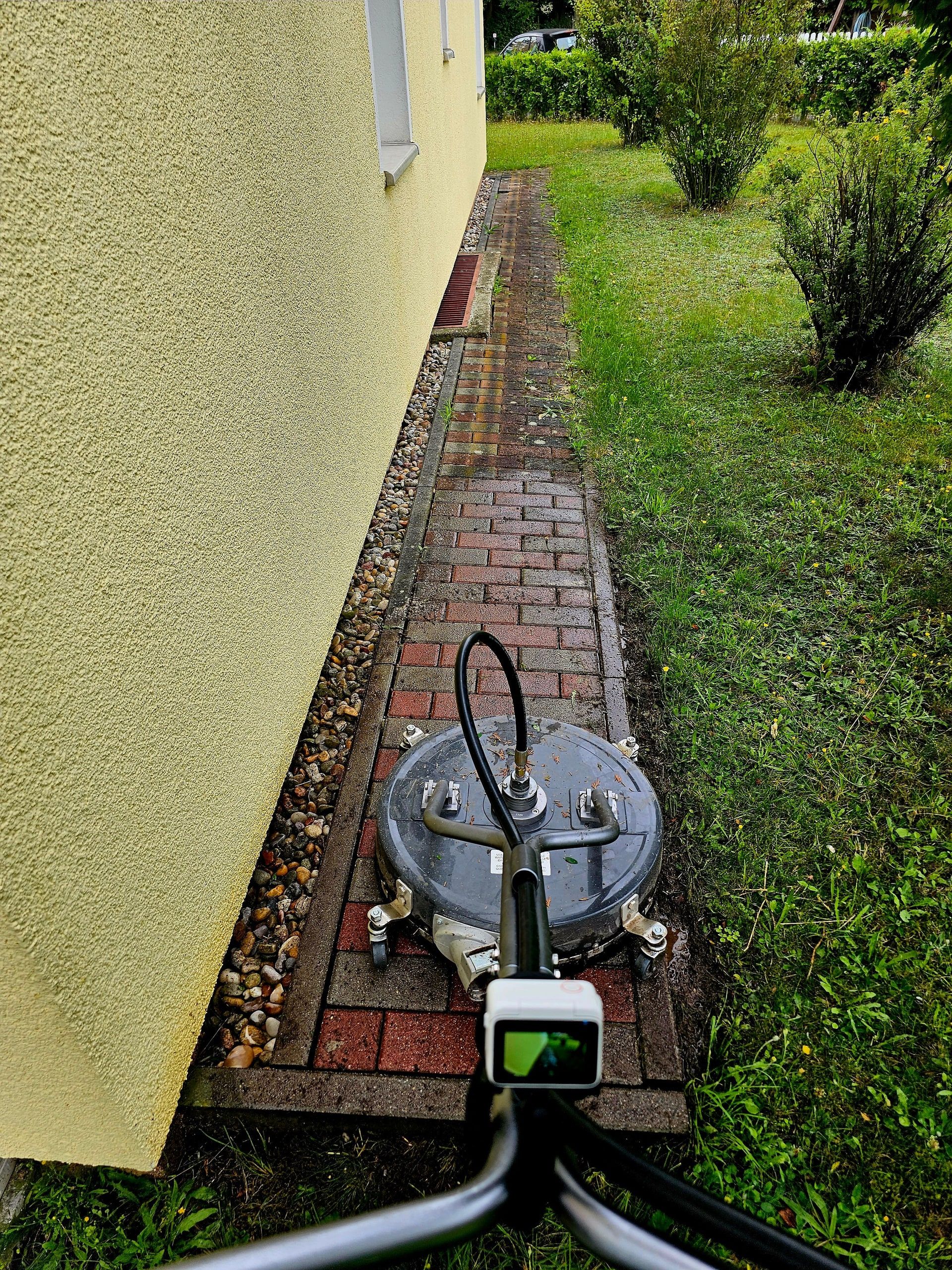 Flächenreiniger auf dem schmalen Klinkerweg zwischen Hauswand und Rasen