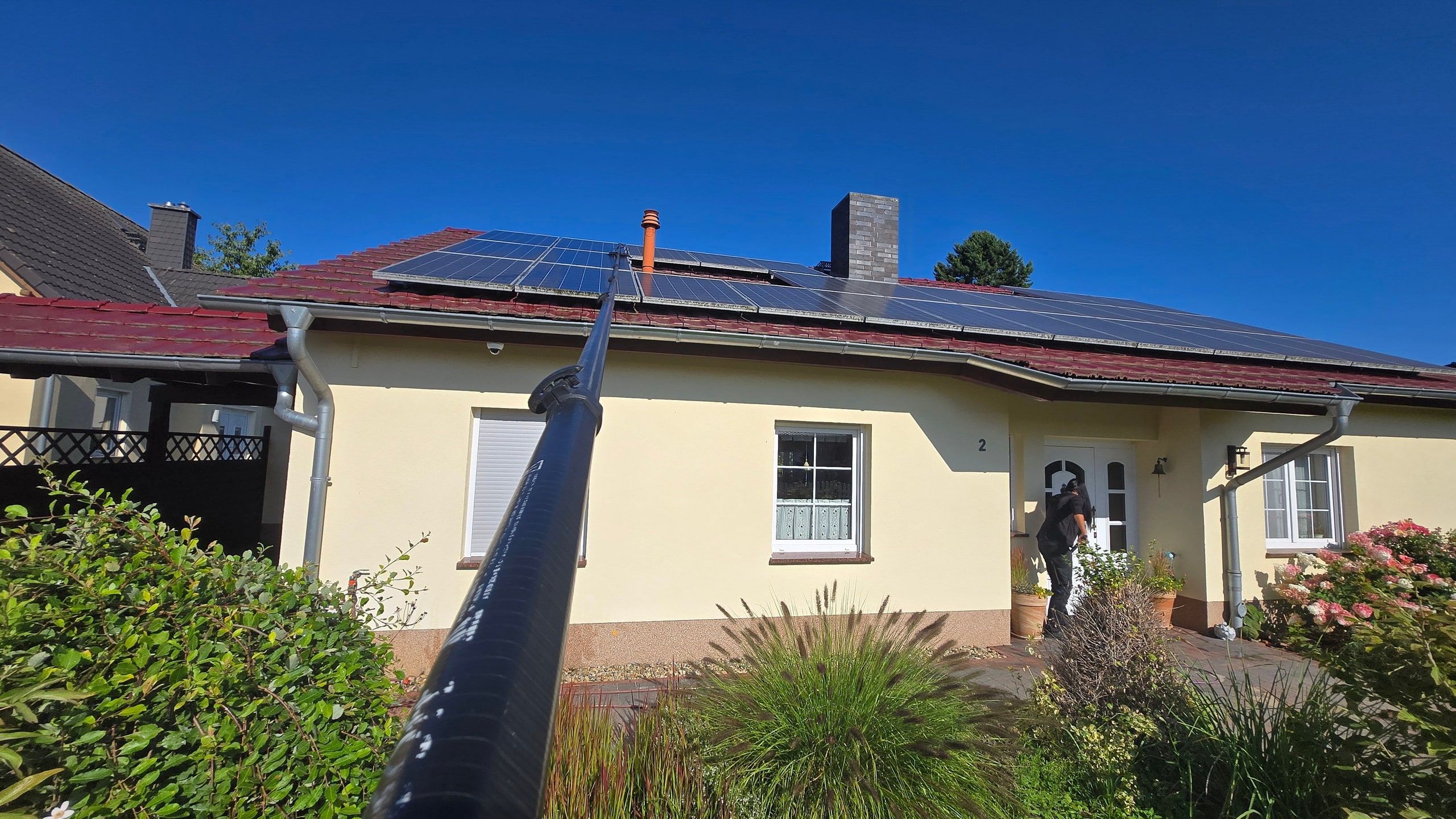 Blick entlang der Teleskopstange auf ein Wohnhaus mit Photovoltaikanlage
