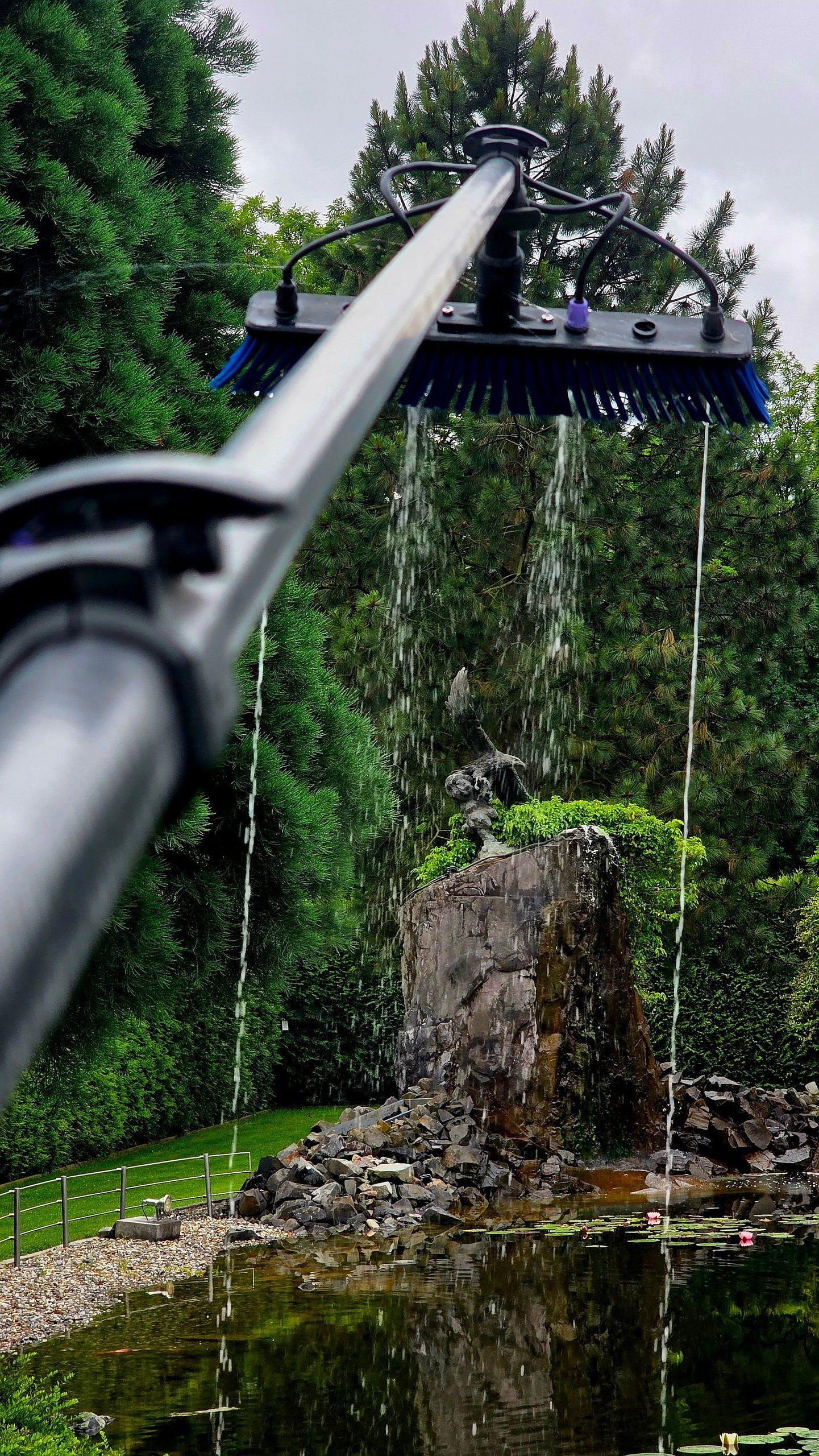Wasserführende Bürste im Einsatz über einem Gartenteich mit Wasserfall