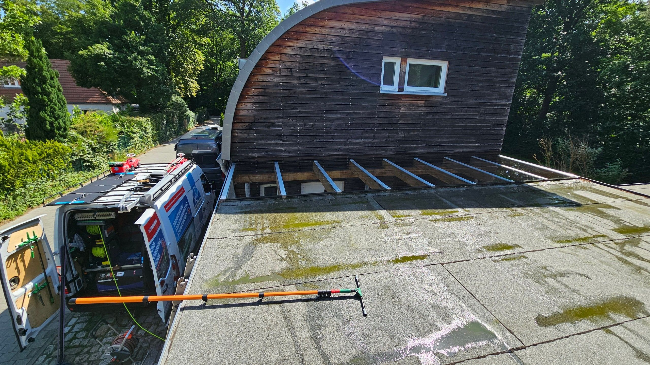 Gereinigtes Glasdach neben einem Tonnendachhaus, links das Einsatzfahrzeug
