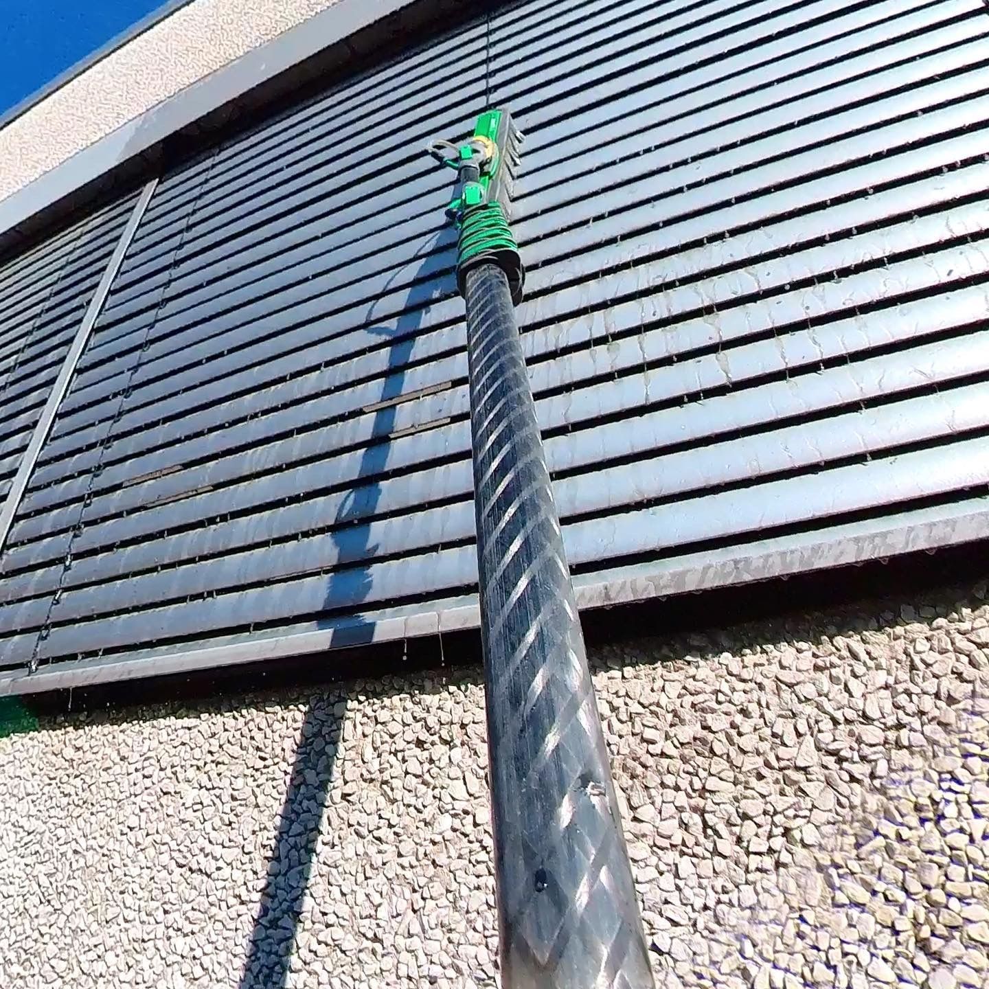 Reinwasserbürste an der Teleskopstange reinigt die Raffstore-Lamellen einer Fassade