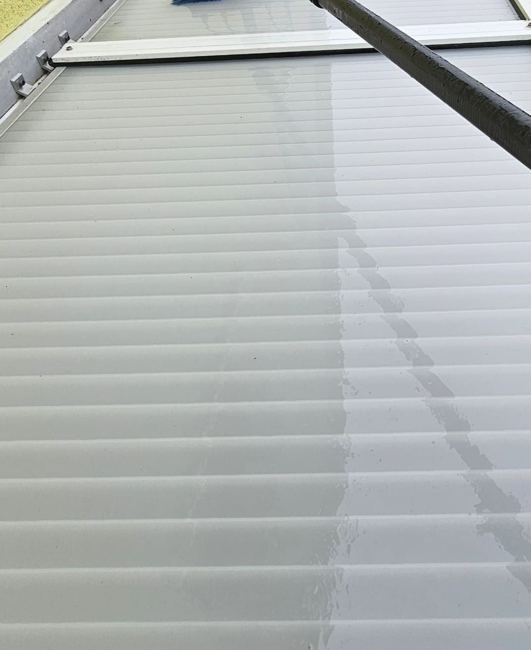 Dasselbe Lichtplattendach nach der Reinigung: die Wellplatten sind wieder hell und lichtdurchlässig, die Aluminiumrahmen sauber, an der Carbonstange läuft klares Wasser ab