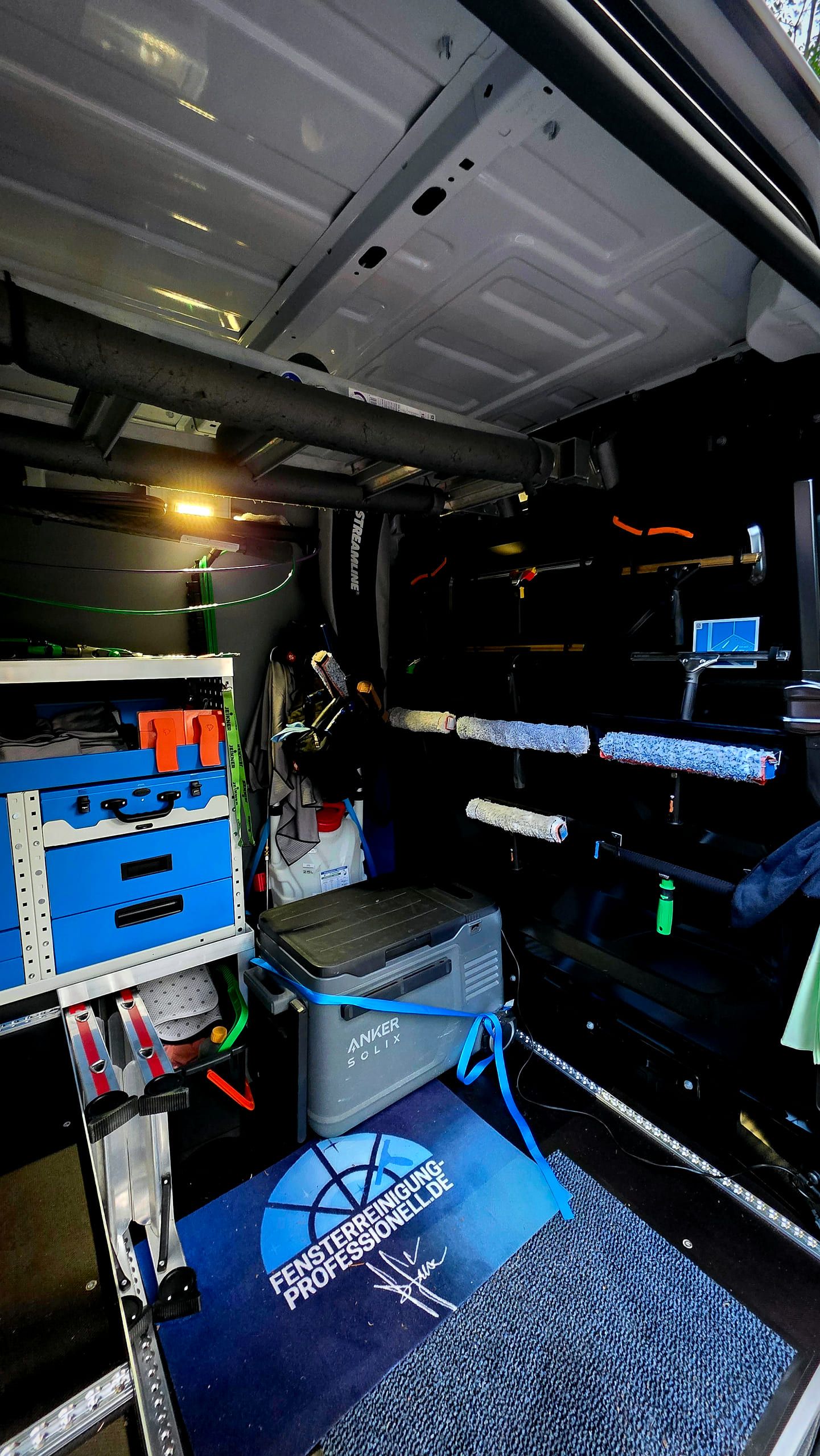 Innenraum des Transporters mit Regalsystem, Werkzeugwand mit Einwaschern und einer Fußmatte mit dem Logo von Fensterreinigung Professionell