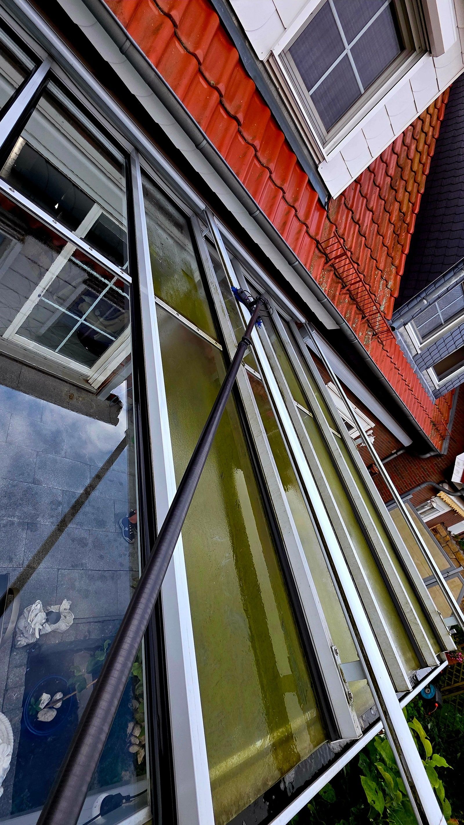 Reinigungsstange an einem bemoosten Glasdach einer Terrassenüberdachung, Aufnahme von oben